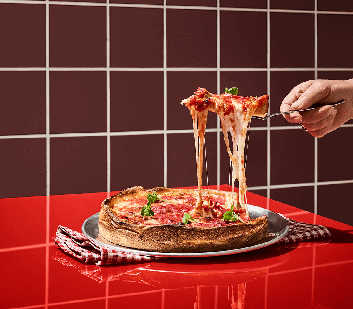 Pizza med höga kanter på tallrik på rött bord med en slice med smält ost som hänger ned från pizzaspade