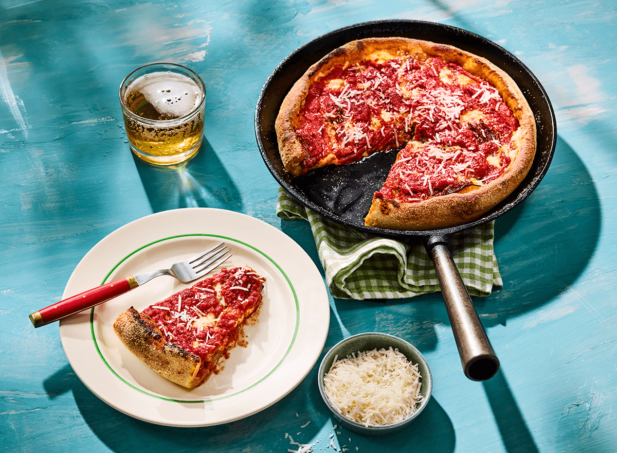 Pizza med höga kanter i panna samt vit tallrik med en pizzaslice och gaffel