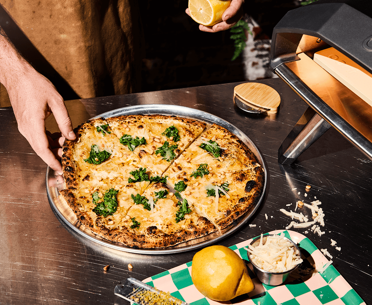 Hand som sträcks mot en gräddad pizza i metallform på blankt bord